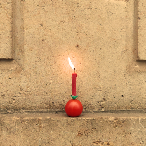 Eine kleine rote Geburtstagskerze, die in einer Kirschtomate steckt, hat eine nach links geneigte Flamme.