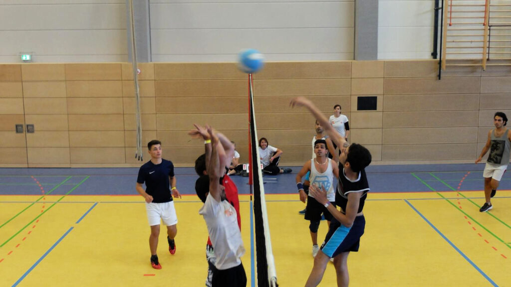 Menschen unterschiedlichen Alters spielen in einer Turnhalle Volleyball.