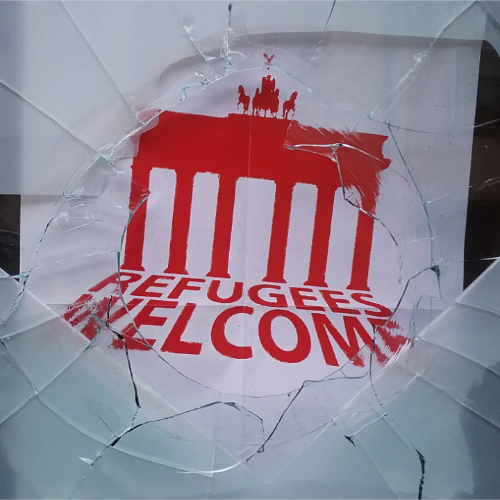 Nahaufnahme von einer zerstörten Scheibe und einem Refugees-Welcome-Plakat