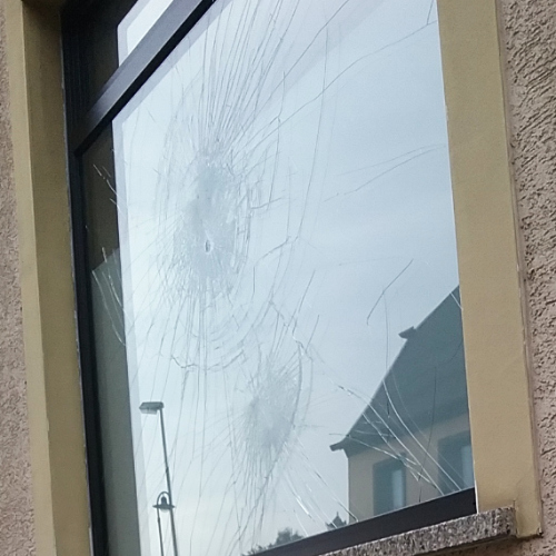beschädigtes Schaufenster, in dem sich ein Hausdach und Laternen spiegeln