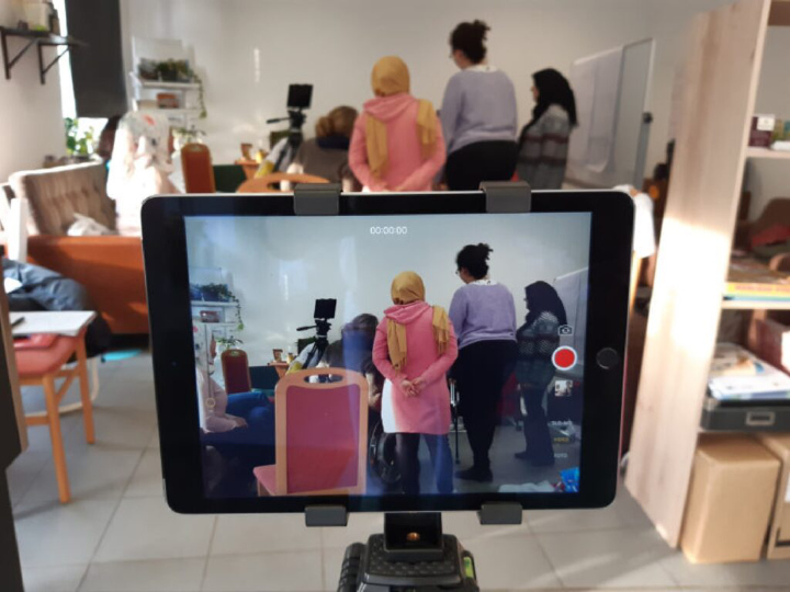 Die Video-Funktion eines Tablets ist aktiv. Es nimmt gerade eine Gruppe von Frauen im Hintergrund des möblierten Büros auf, die sich besprechen. Einige der Frauen tragen Kopftuch.