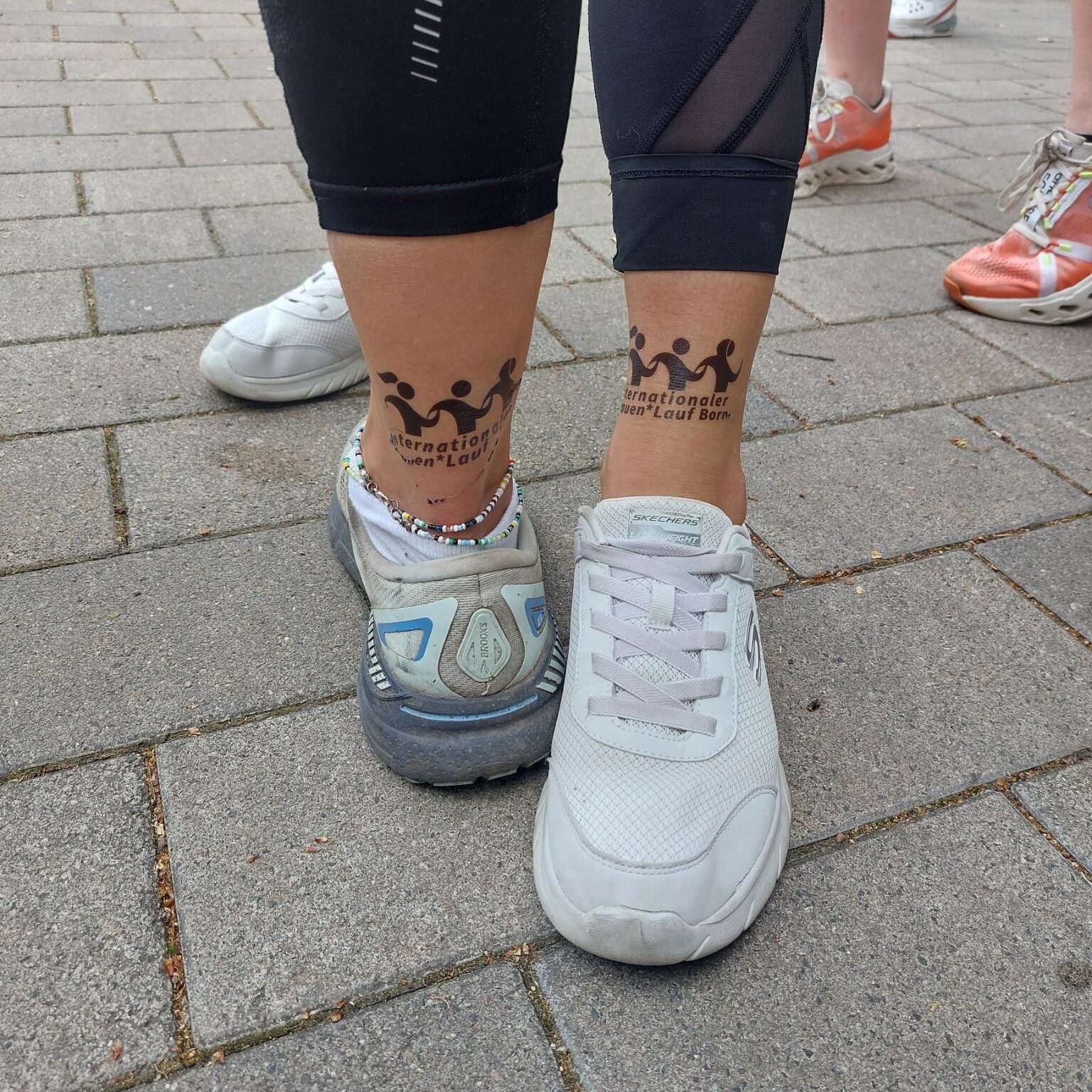 Zwei verschiedene Beine präsentieren das schwarzene Tattoo des Internationalen Frauenlauf Borna. Einmal ist es hinten oberhalb der Ferse und einmal vor oberhalb des Fußes angebracht.