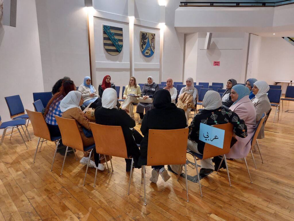 In einem Stuhlkreis sitzen weiblich gelesene Personen zusammen, die mehrheitlich verschieden farbige Kopftücher tragen.
