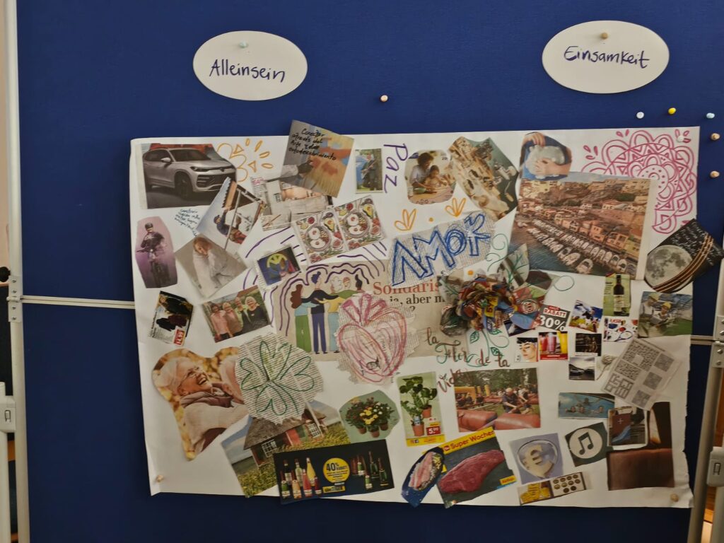 Eine Collage mit vielen verschiedenen bunten, aus Zeitungen ausgeschnittenen Bildern hängt an einer blauen Pinnwand und ist zusätzlich mit kleineren Wörtern und Zeichnungen gestaltet. Über der Collage sind auf zwei weißen Karten Alleinsein und EInsamkeit getrennt voneinander gepinnt.